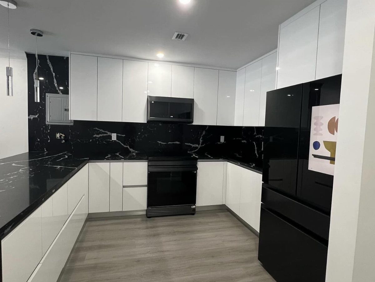 Modern kitchen with glossy white cabinets, black marble countertops, and black appliances.
