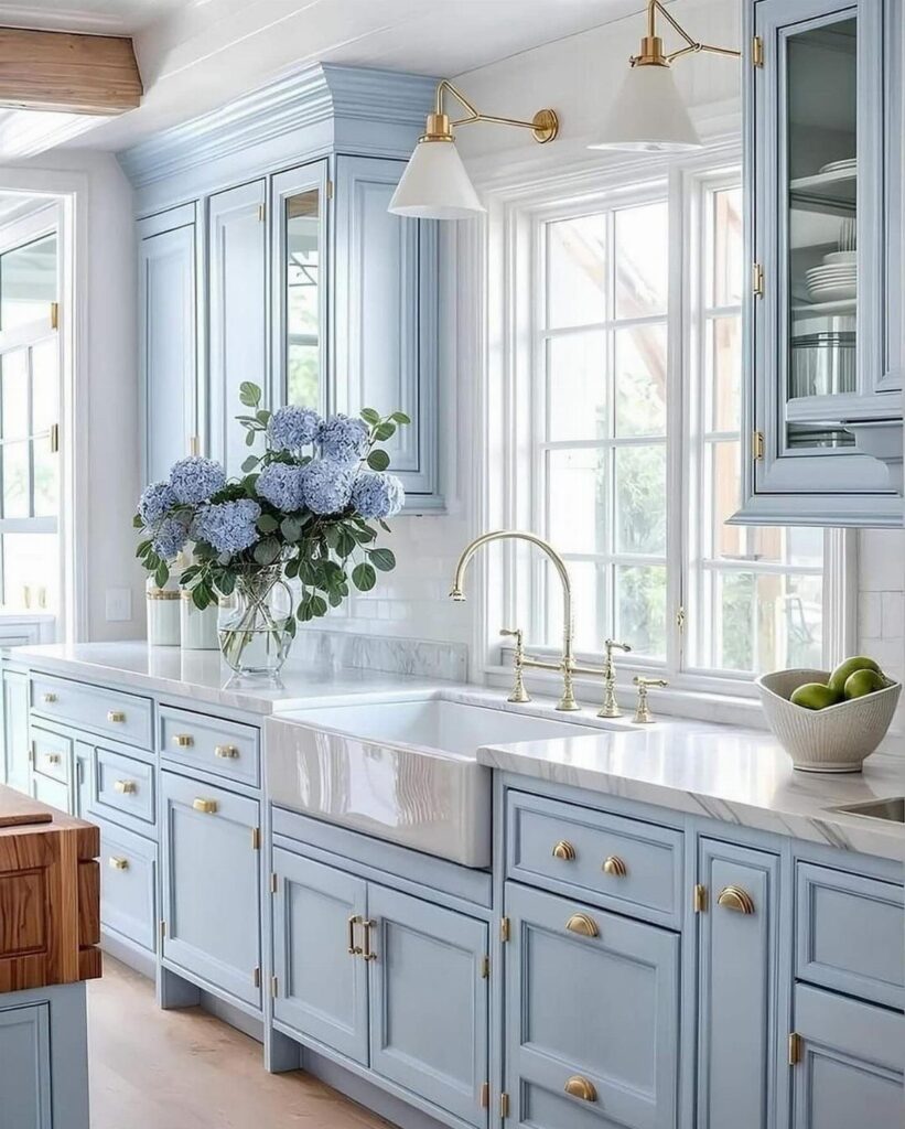 Light blue kitchen cabinets with gold hardware and white marble countertops.