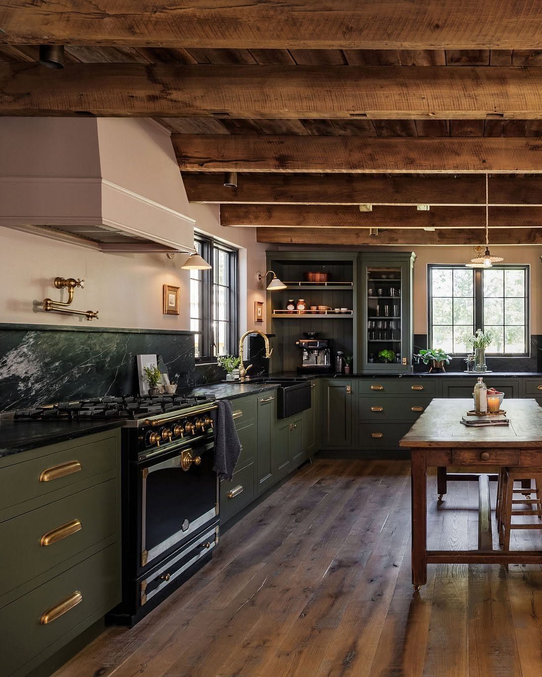 Dark green kitchen cabinets with gold hardware under rustic exposed wooden ceiling beams.