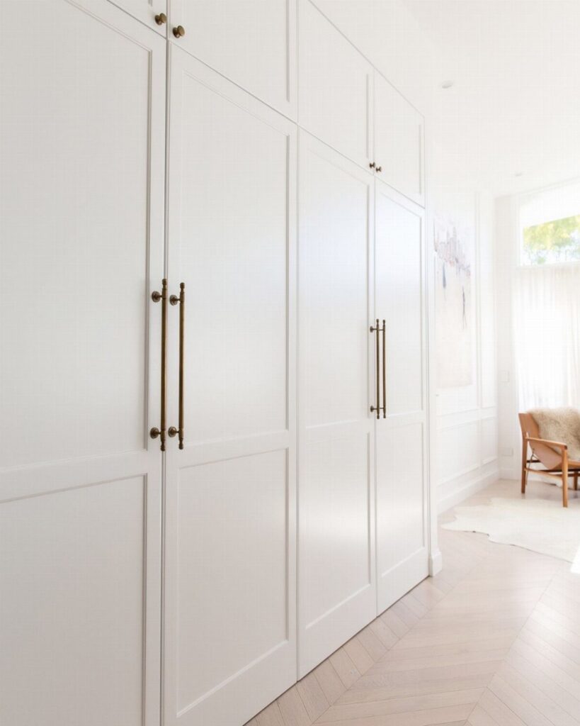 White floor to ceiling cabinets with gold handles in a bright herringbone hallway