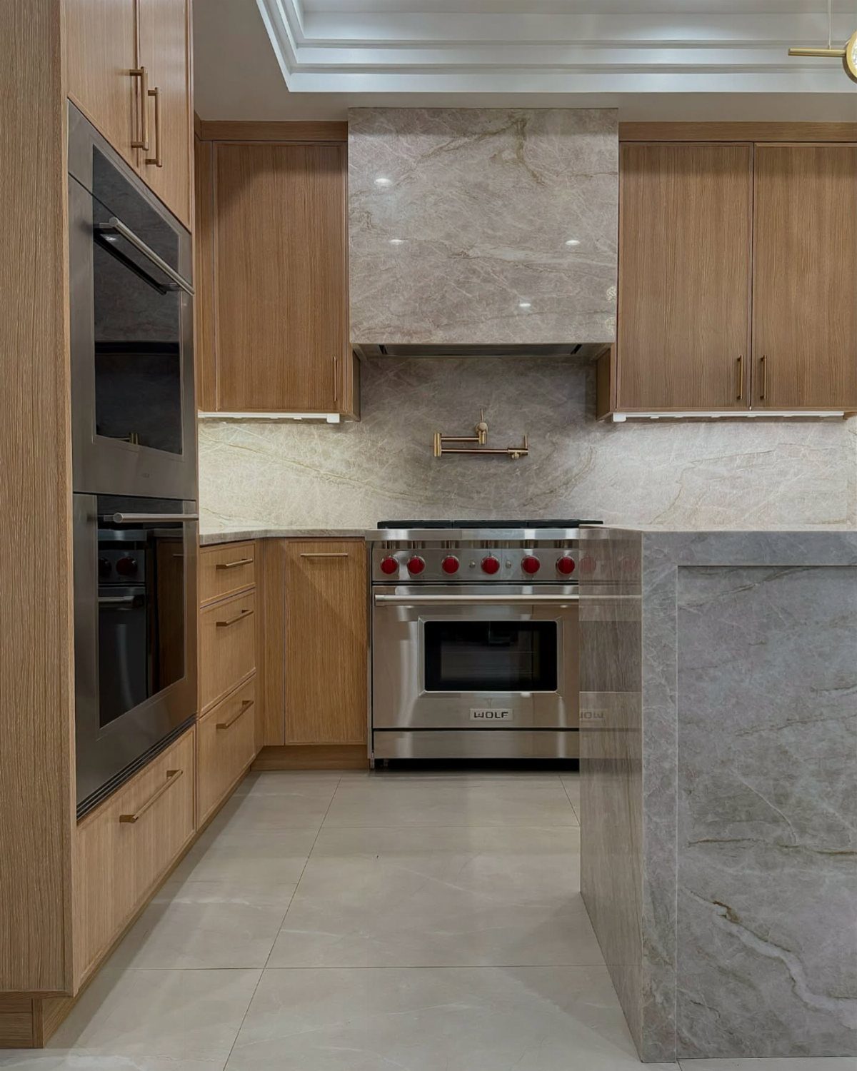 Modern luxury kitchen with light wood cabinets and grey marble surfaces.