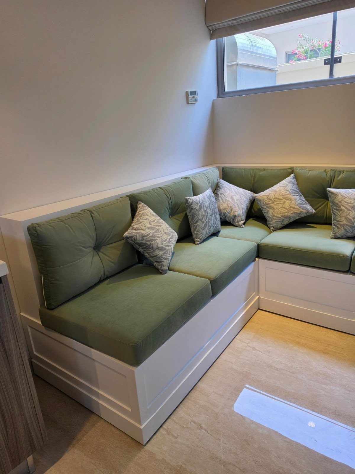 White built-in L-shaped kitchen bench with green cushions and grey patterned pillows.