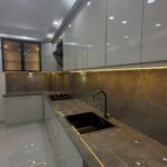 Polished grey veined porcelain countertops and backsplash with glossy white kitchen cabinets.