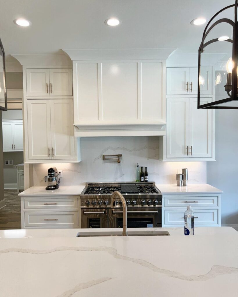 White kitchen cabinets and marble countertops surrounding a professional stainless steel gas range.