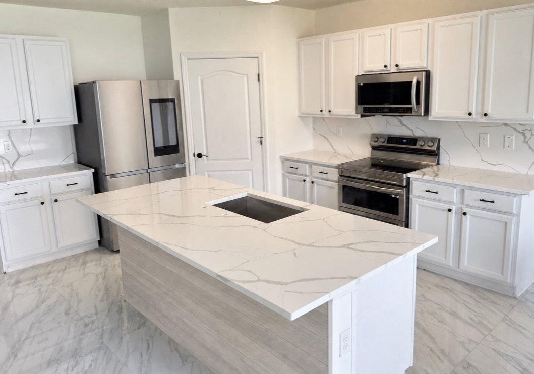 White kitchen cabinets and marble countertops with a matching center island and stainless appliances