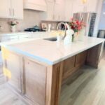Kitchen island with white marble countertop and light brown wood paneled back panel.