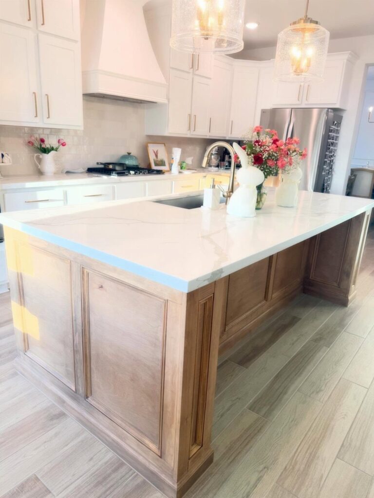 Kitchen island with white marble countertop and light brown wood paneled back panel.