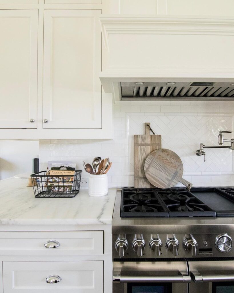 Off-white kitchen cabinets with marble countertops and a professional stainless steel gas range.