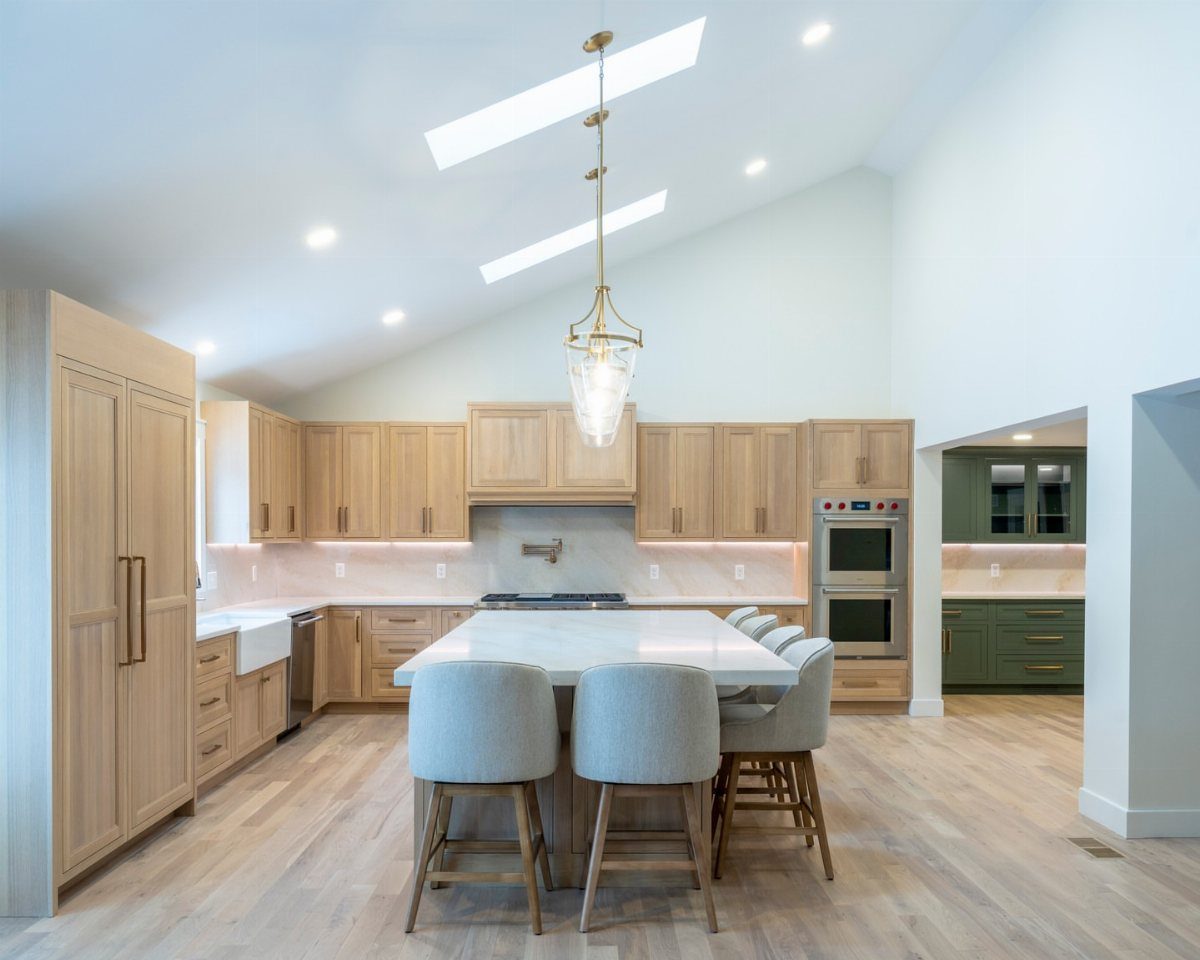 Modern kitchen with light wood cabinetry, white marble island, and high vaulted ceilings.