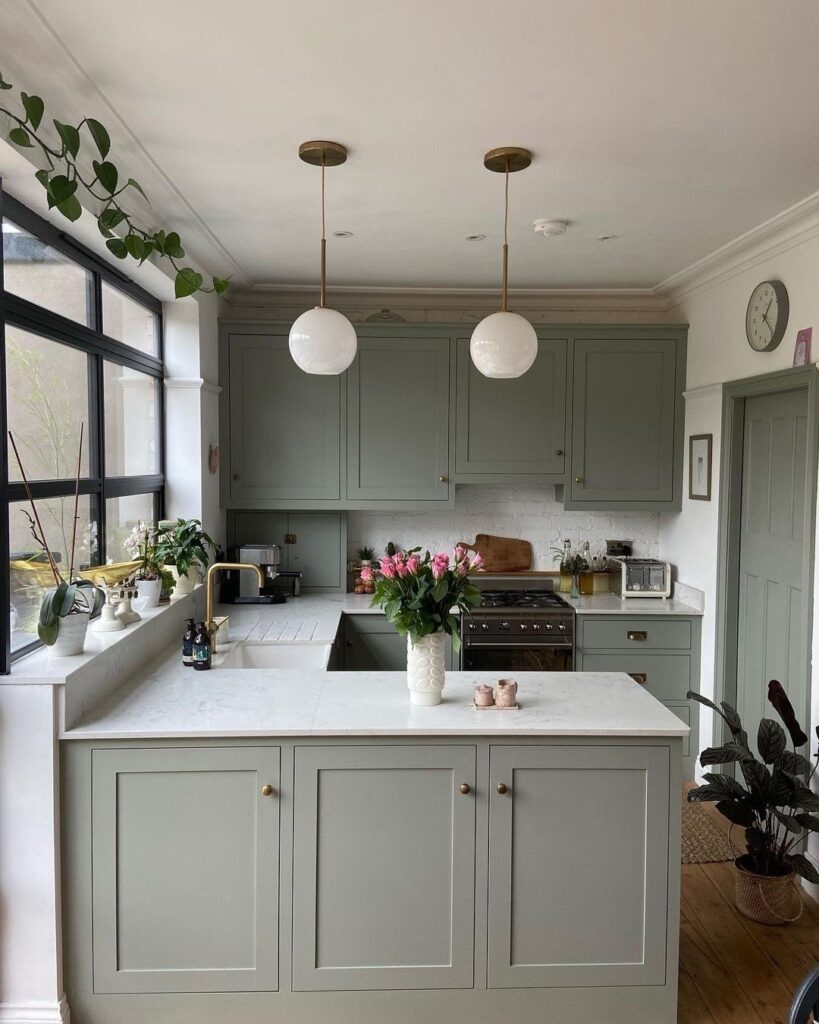 Sage green kitchen with a small white marble island and globe pendant lights.
