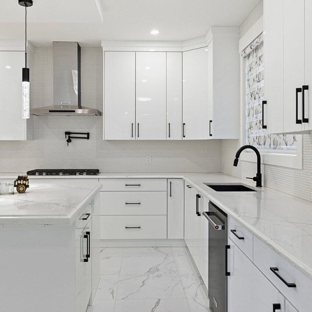 Modern kitchen with glossy white cabinets, marble countertops, and black hardware accents.