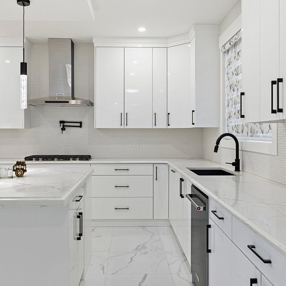 Modern kitchen with glossy white cabinets, marble countertops, and black hardware accents.