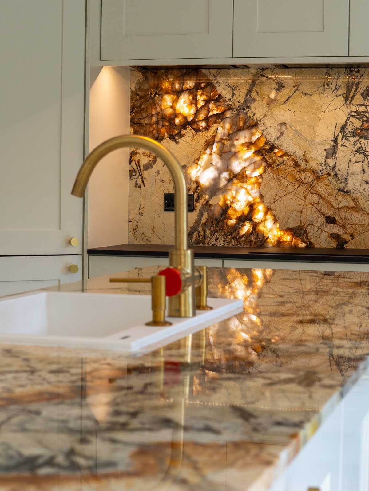 Backlit natural stone backsplash and matching countertop with a gold kitchen faucet.