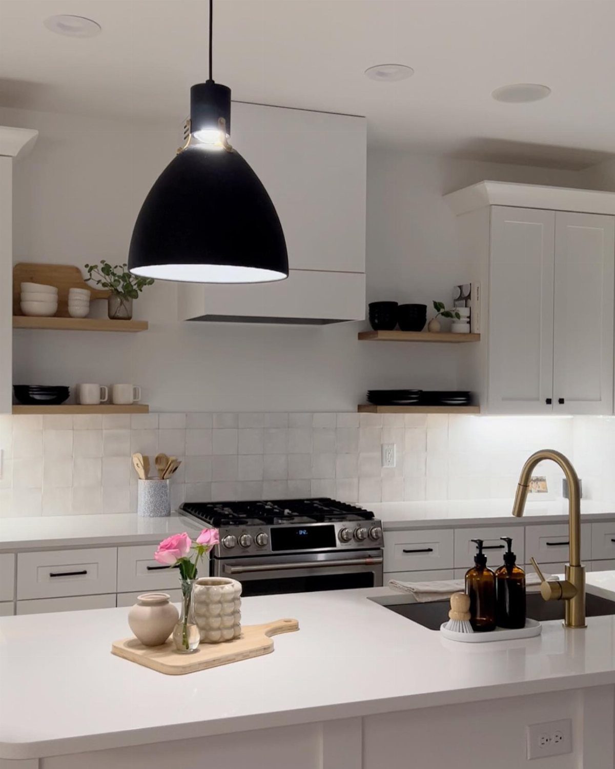 Modern white kitchen with light wood open shelving and a black pendant light.