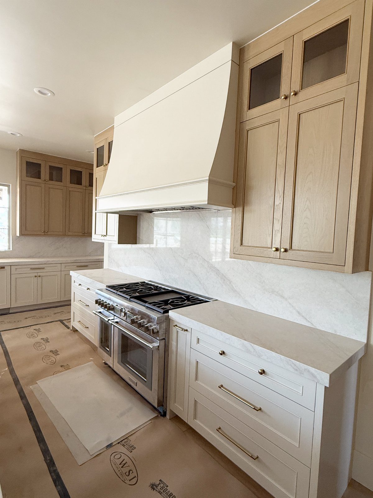 Greige upper cabinets and white lower cabinets in a modern kitchen with marble countertops.