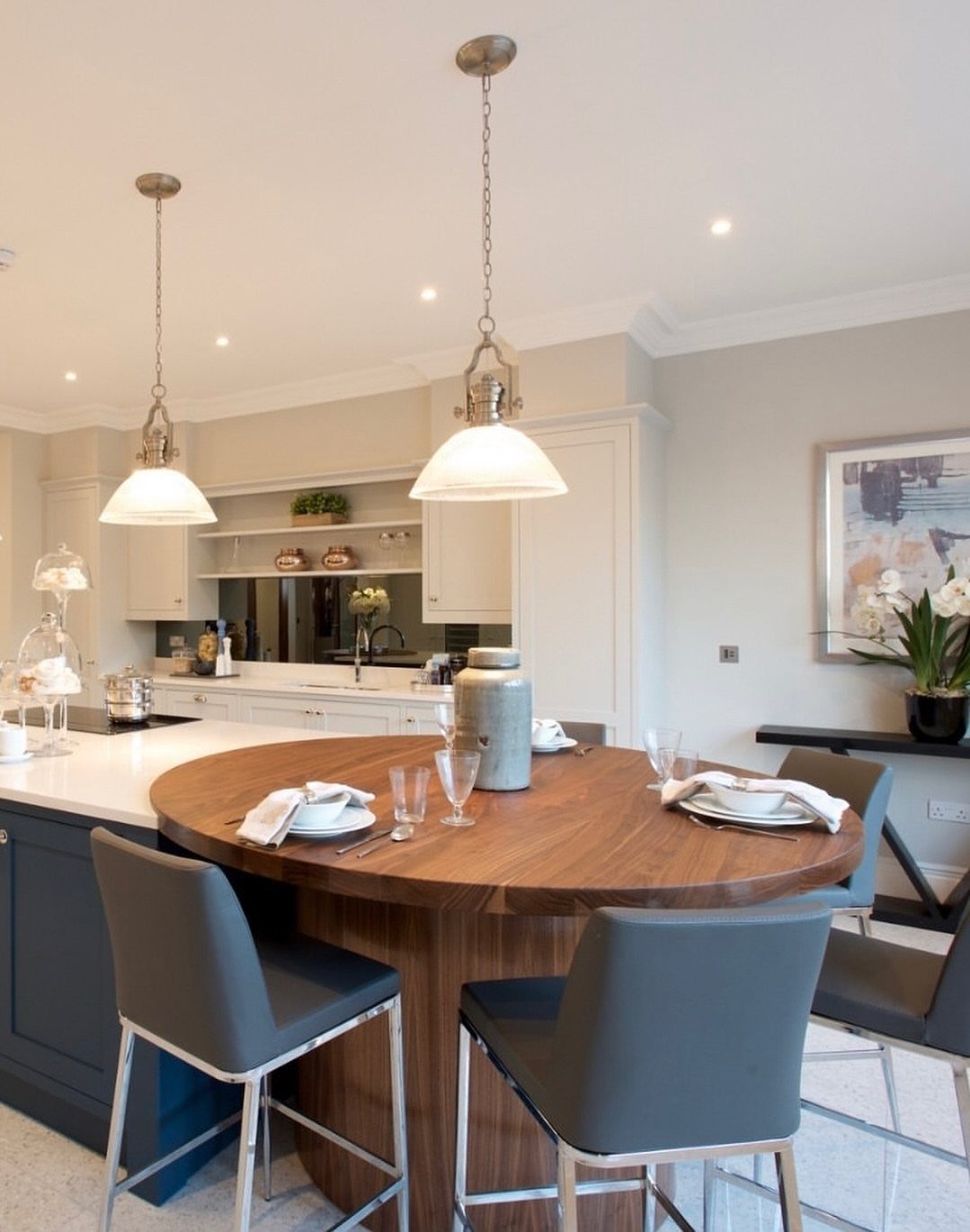 Round wooden dining table attached to a blue kitchen island with grey chairs.