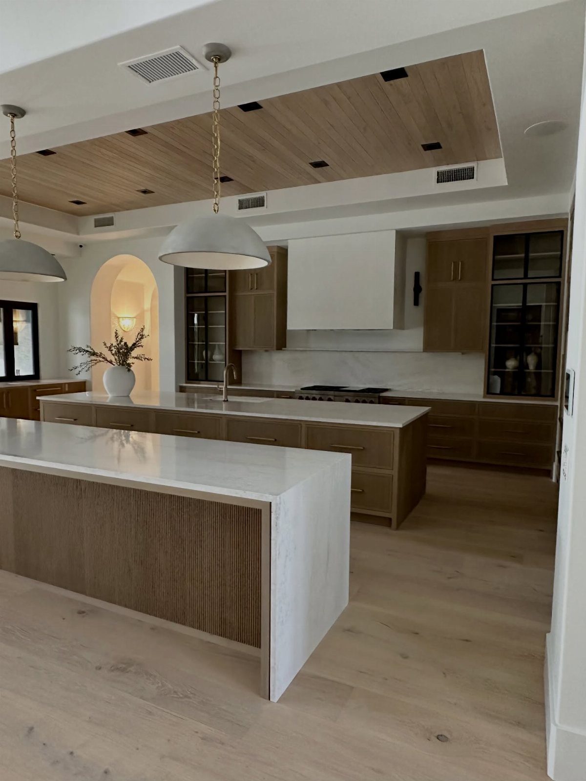 Two level kitchen island with white countertops and light wood cabinetry and flooring.