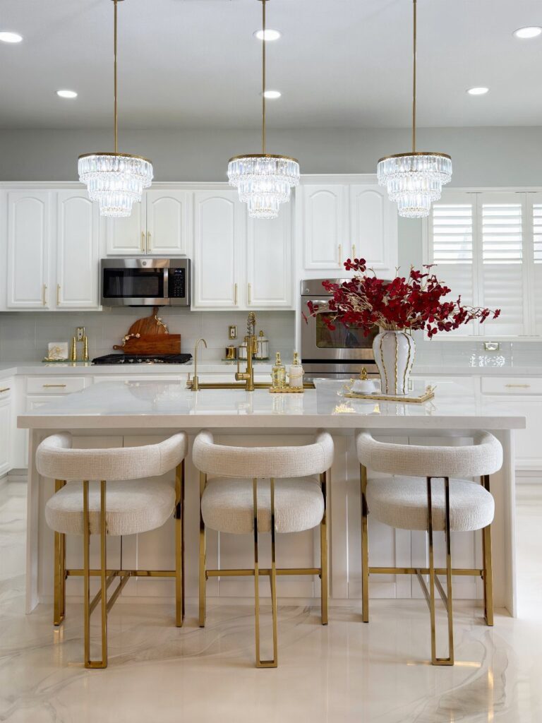 White and gold kitchen with crystal chandeliers and white upholstered barstools.